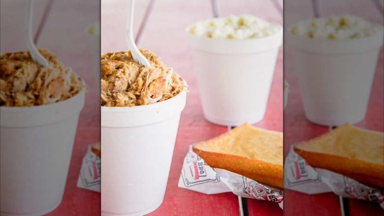 Styrofoam containers of pulled pork and salad with bread on a red picnic table