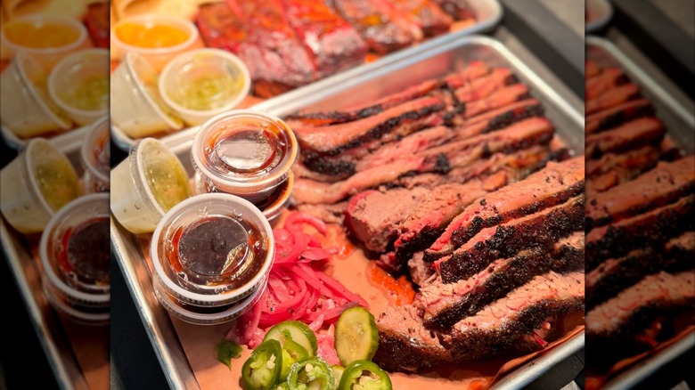 Tray of sliced brisket with sauce cups, jalapeños, and onions