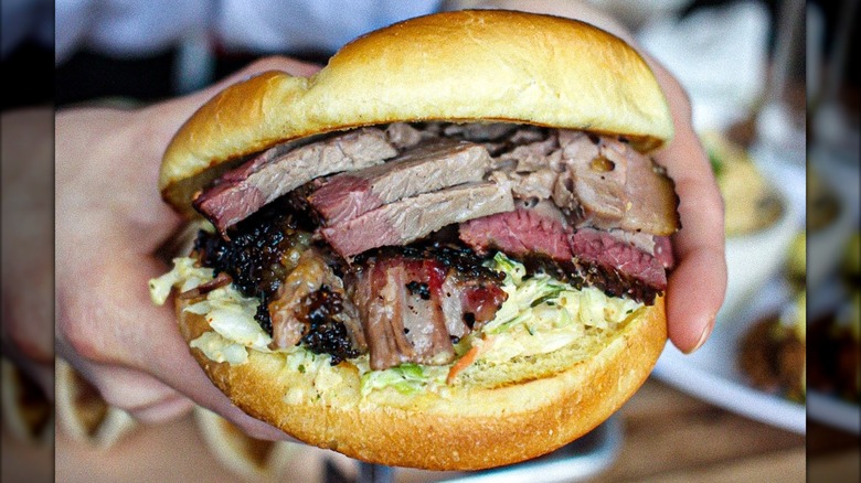 Hands holding a brisket sandwich with slaw