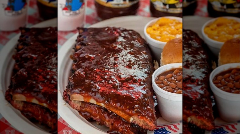 Saucy ribs on a plate with beans, a roll, and mac and cheese