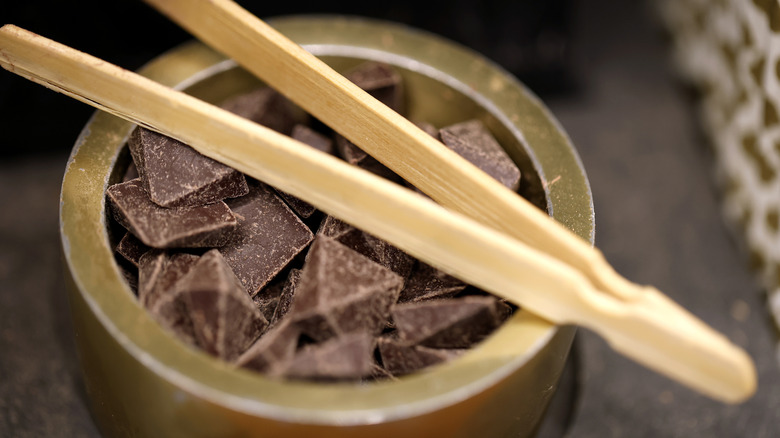 A close up of a small bowl of chocolate samples at Dandelion Chocolate with a wooden serving tongs