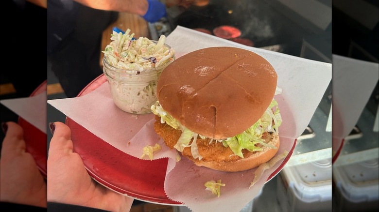 Hand holding red plate with fish sandwich and side of cole slaw