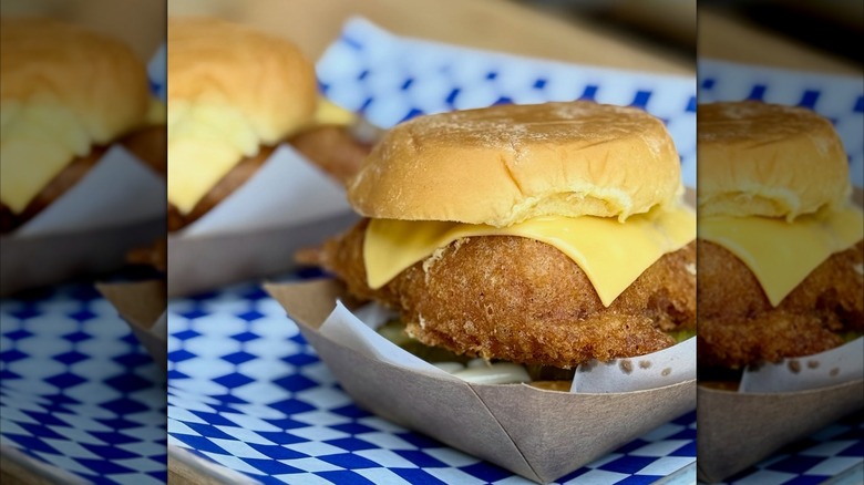 Fish sandwich with cheese in basket on blue and white checkered tablecloth
