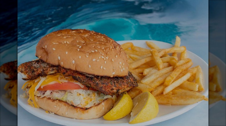 Fish sandwich next to fries and lemon slices on white plate