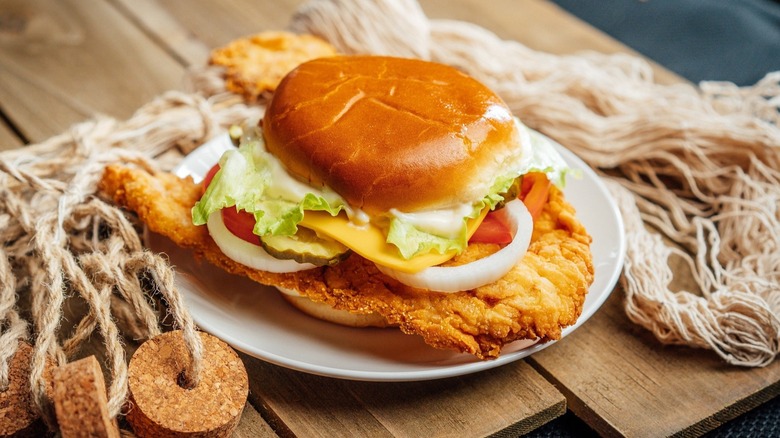 Fish sandwich with onion, tomato, cheese on white plate