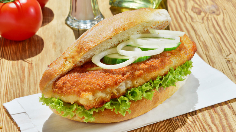 Fish sandwich on hoagie roll with onions, cucumbers on wood table