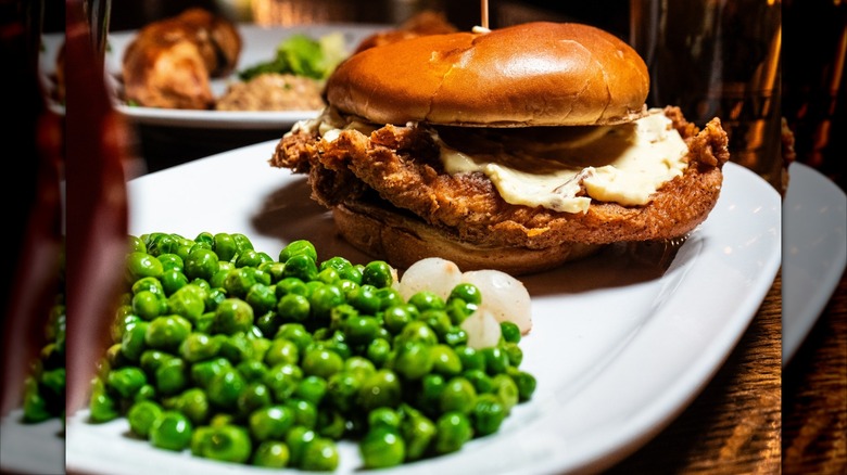 Fried fish sandwich and peas on white plate