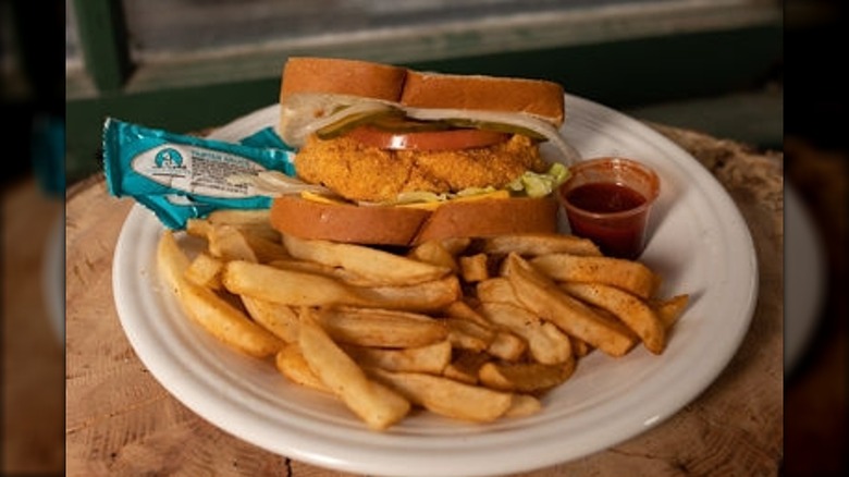 Fish sandwich, fries, and sauces on white paper plate