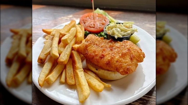 Open-faced fish sandwich next to fries on white plate