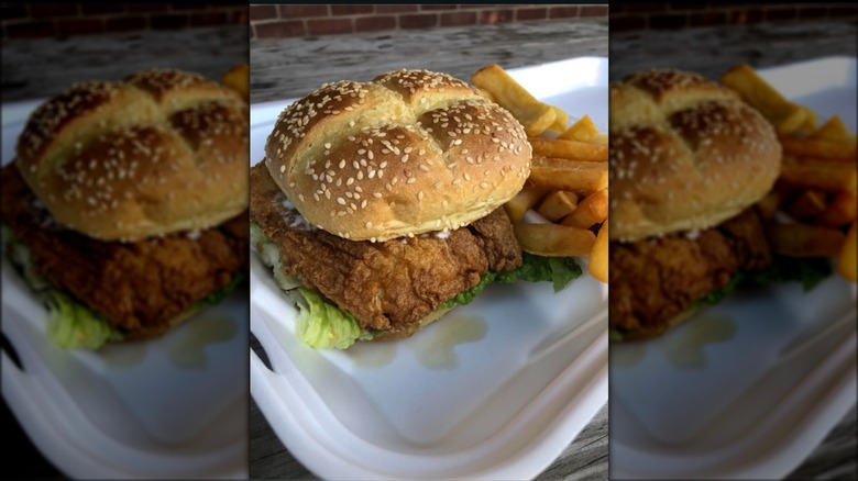 Fried fish sandwich on seeded bun and fries in white takeout container