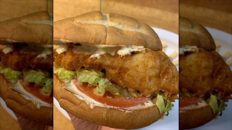 Fish sandwich with shredded lettuce, tomato, tartar sauce on bun