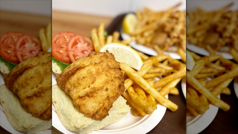 Open-faced fish sandwich next to fries and lemon wedge on white paper plate