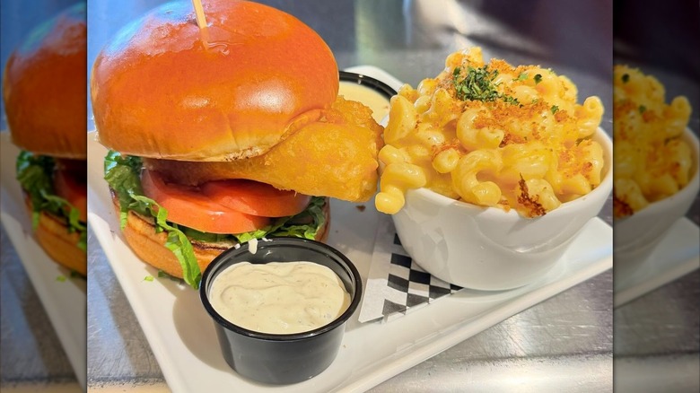 Fish sandwich next to cup of mac and cheese topped with breadcrumbs