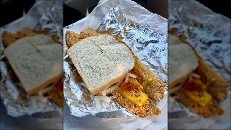 Two large fish fillets sandwiched between white bread on aluminum foil
