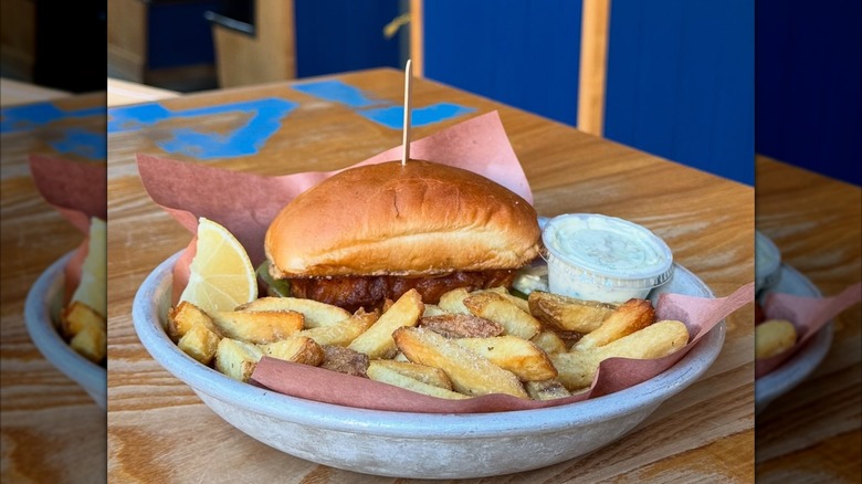Browned roll with fish sandwich and french fries in white bowl
