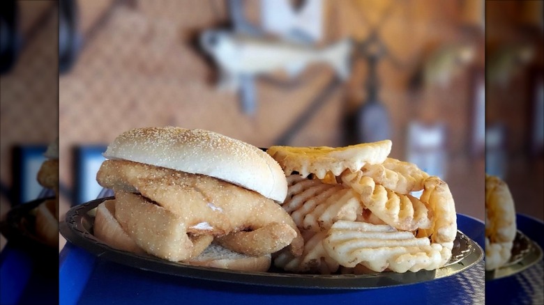 Fish sandwich on burger bun next to plate of waffle fries