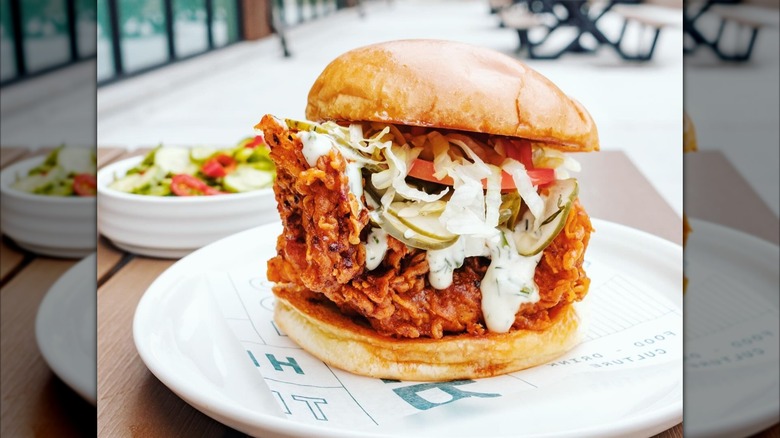 Fish sandwich with tartar sauce, lettuce, tomatoes on white plate