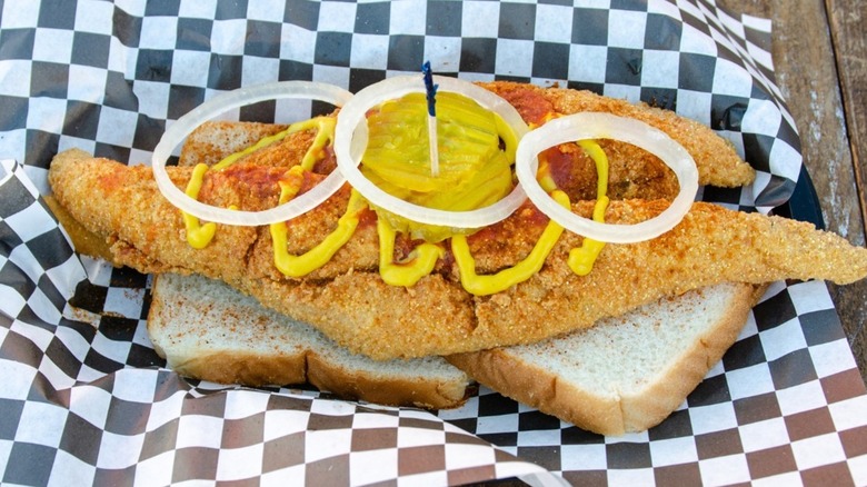 Open-faced fish sandwich with mustard, pickles, onion on white bread