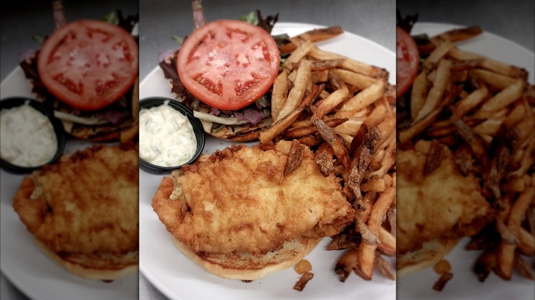 Open-faced fish sandwich with tomato next to french fries on white plate