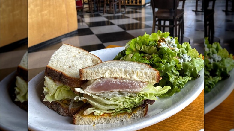 Grilled tuna sandwich with lettuce on white bread next to salad