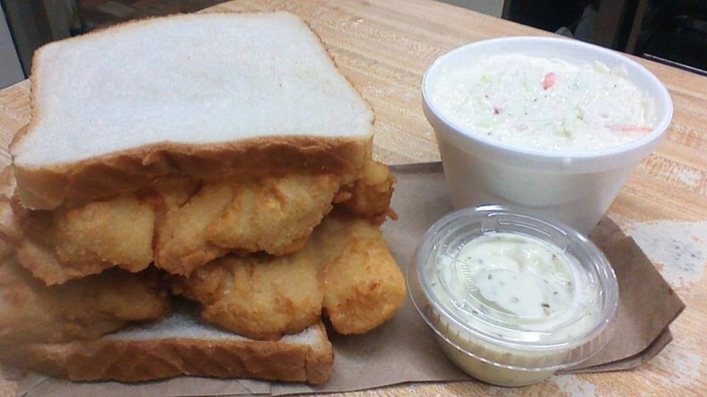 Fish sandwich next to coleslaw on brown paper bag