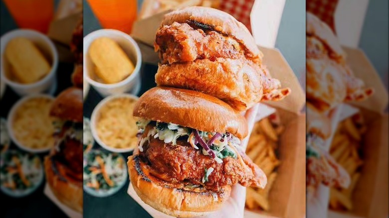 Two Nashville hot chicken sandwiches with fries and sides in blurred background