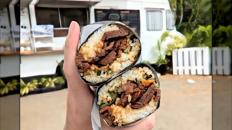 Hand holding beef wraps in front of food truck