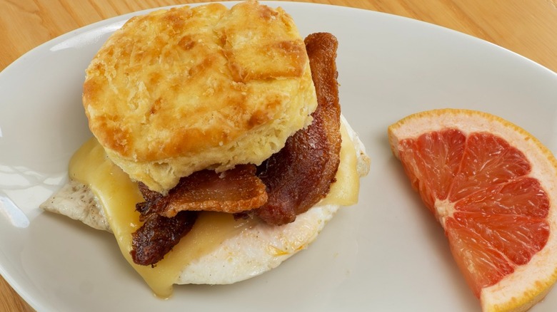 Biscuit breakfast sandwich with bacon and slice of grapefruit