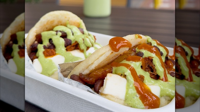 Two arepas with sauces in takeout container