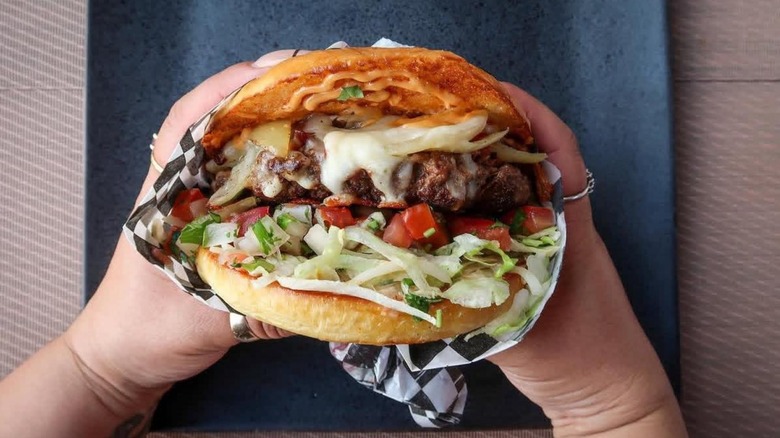Two hands holding a massive burger with lettuce, cheese, tomato