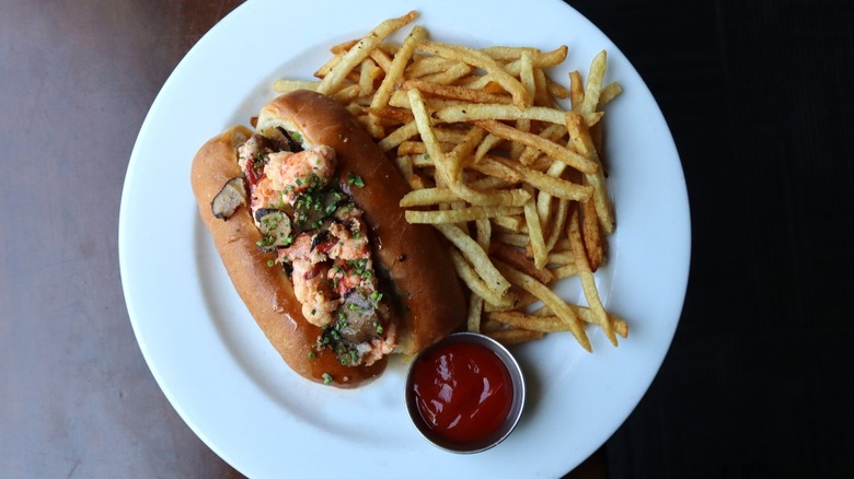 Top-down shot of lobster roll and fries on white plate