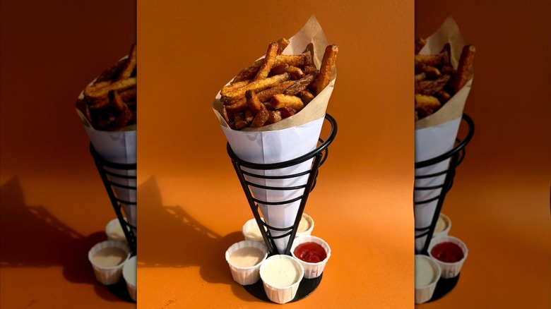 Cone of fries surrounded by sauces on orange background
