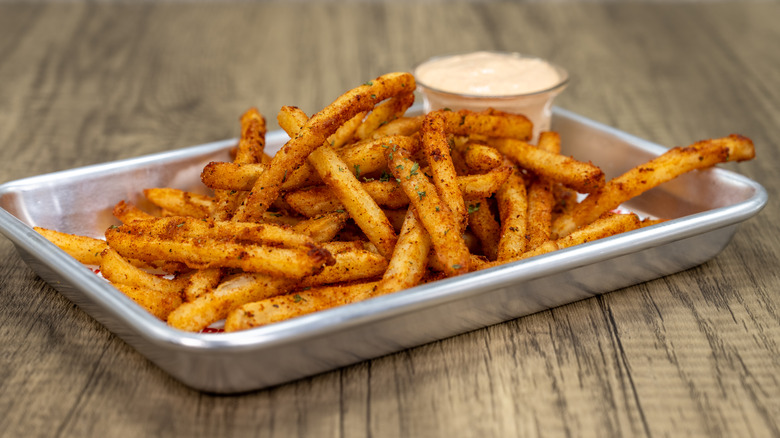 Metal tray of crispy cajun fries and sauce on wooden table