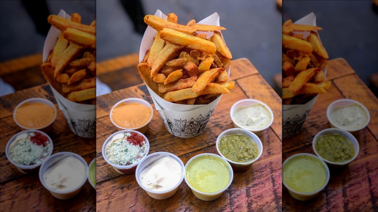 Cup of fries surrounded by dipping sauces on wooden table