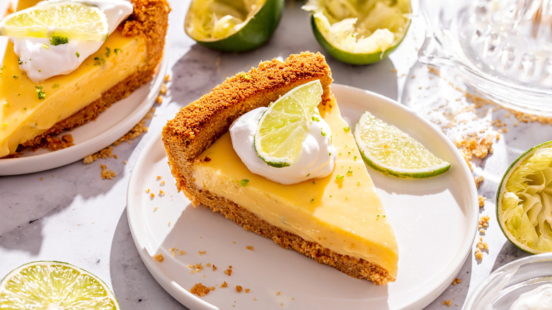 piece of Key lime pie with graham cracker crust, whipped cream, and a lime slice garnish