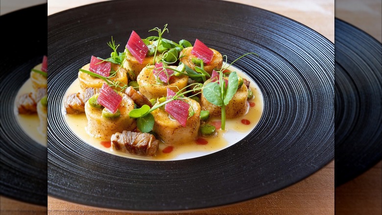 Ricotta gnudi with lamb and greens on blac plate