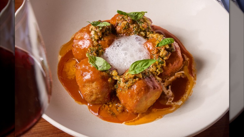 Veal meatballs with sauce in white dish with red wine in foreground