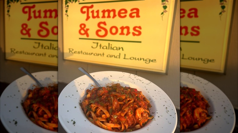 Seafood fettucinie in white bowl in front of restaurant sign