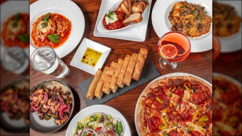 Assortment of Italian dishes, bread, olive oil, pizza, and salad on wood table