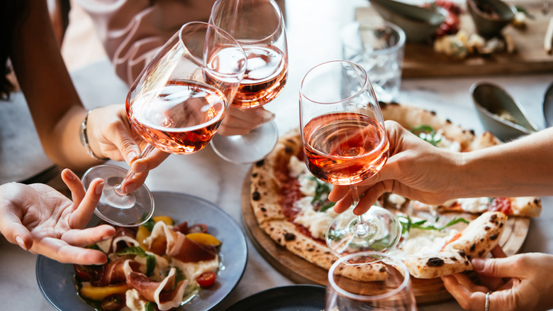 Diners holding wine glasses over table with wood-fired pizza