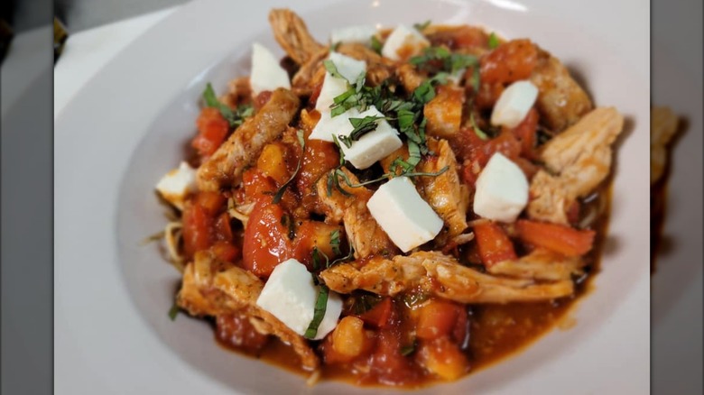 Pasta dish with cheese, tomatoes, and chicken in white bowl