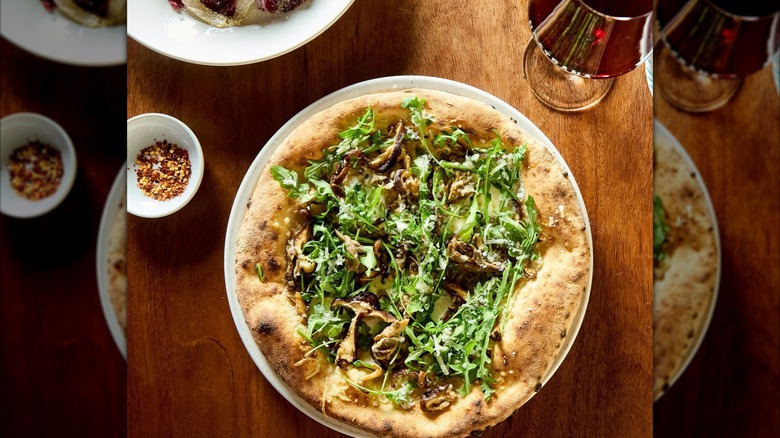 Mushroom pizza with greens on wooden table
