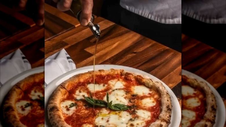 Hand drizzling olive oil on a wood-fired pizza