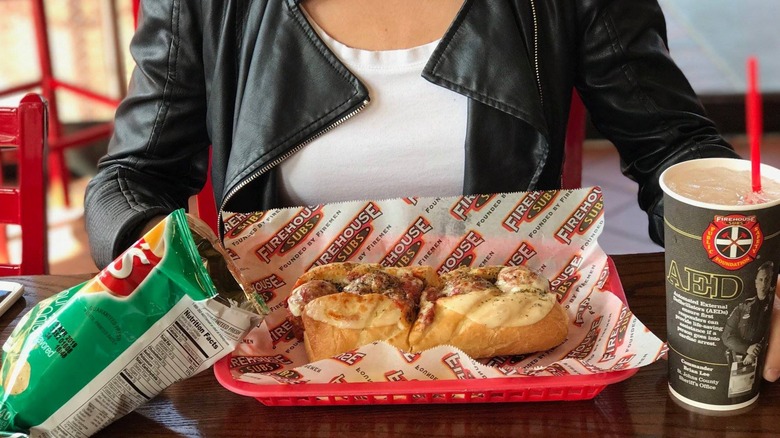 Meatball sub from Firehouse in red plastic tray with soda and bag of chips