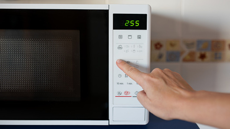 a finger touches the keypad of a microwave oven