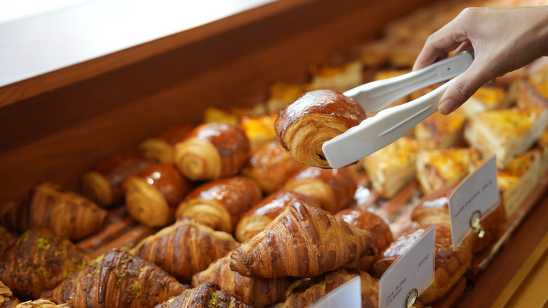 Someone pulling a pain au chocolat pastry from a bakery display case.