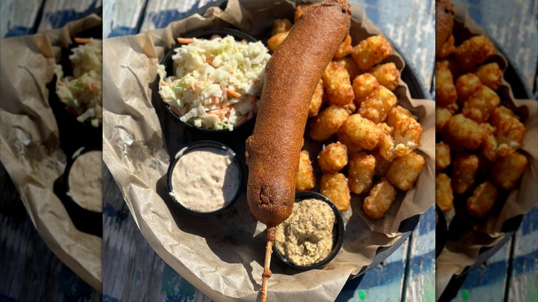 Conecuh sausage corn dog with tater tots, coleslaw, and mustards on blue table