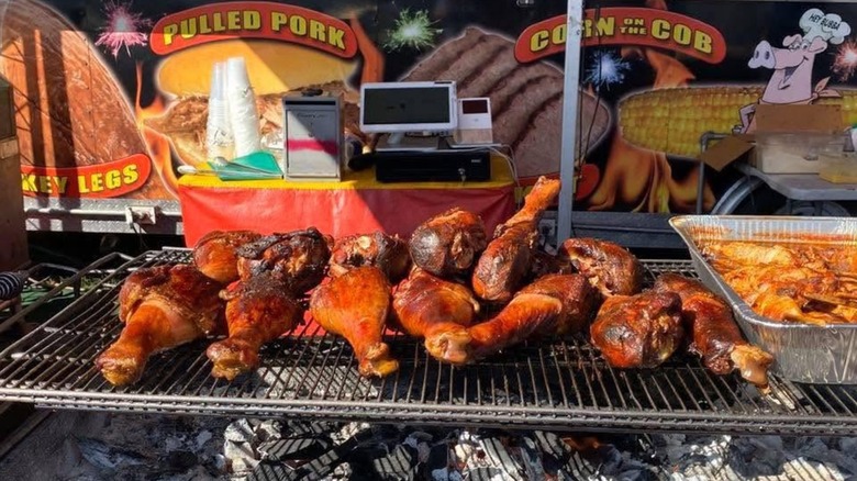 Turkey legs on grill outside in front of stand advertising fair food