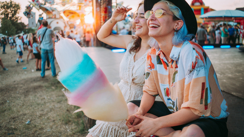 Two happy people with cotton candy and blurred carnival or fair background