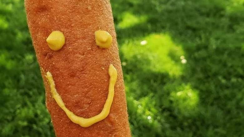 Corn dog with grassy background and smiling mustard face